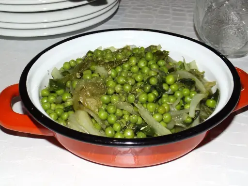 Un plat de petits pois et légumes verts, assaisonnés d'herbes, dans une cocotte orange. Une recette simple et savoureuse.