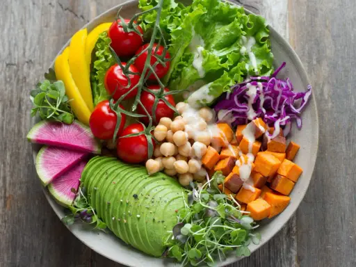 Une assiette colorée avec avocat, tomates, pois chiches, patates douces, chou rouge, radis et poivron jaune. Une belle idée de salade composée.