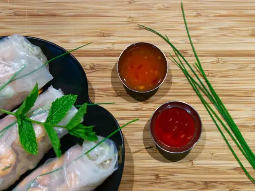 Rouleaux de printemps frais sur une assiette noire, accompagnés de deux sauces : une sauce aigre douce orangée et une sauce rouge.