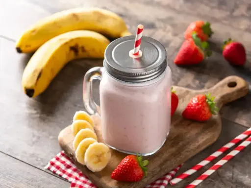 Un délicieux smoothie fraise banane dans un bocal en verre, garni de fruits frais et de pailles rayées.