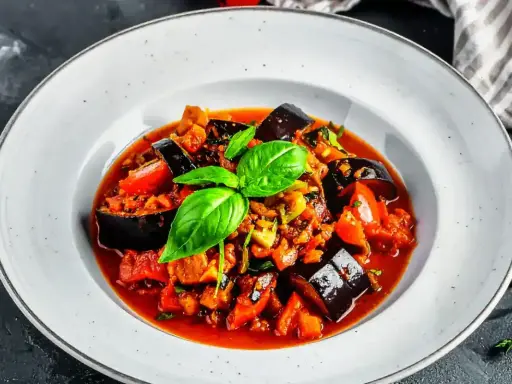 Un plat de ratatouille recette coloré et appétissant, garni de basilic frais, dans une assiette blanche.