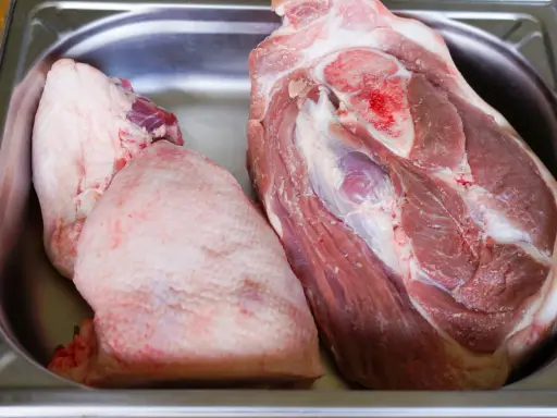 Deux morceaux de viande crue, dont une belle rouelle de porc, reposent dans un bac en métal.