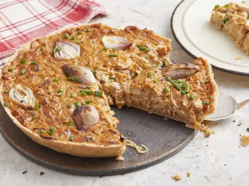 Une délicieuse tarte à l'oignon, garnie d'oignons caramélisés et de ciboulette fraîche, est prête à être dégustée. Une part est servie sur une assiette.
