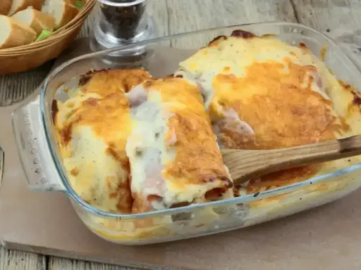 Un plat gratiné de roulés d'endives au jambon, nappés d'une sauce crémeuse et dorée, prêt à être dégusté.