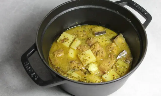 Un plat mijoté de colombo de porc avec des morceaux de pommes de terre et des épices dans une cocotte en fonte noire.
