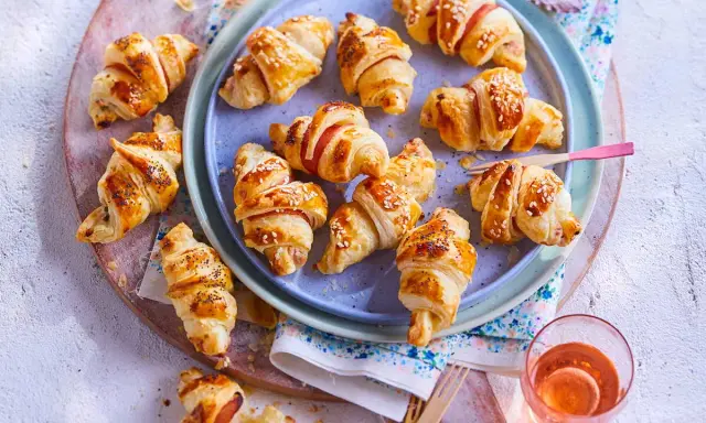 Petits croissants au jambon dorés, certains saupoudrés de graines de sésame ou de pavot, prêts à être dégustés.