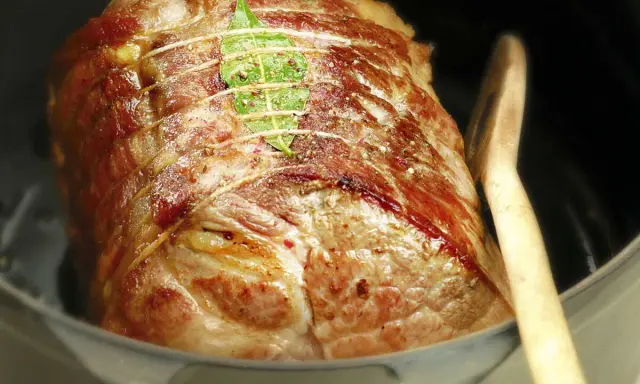 Un rôti de porc cocotte, doré et savoureux, est prêt à être dégusté. Une feuille de laurier orne sa surface.