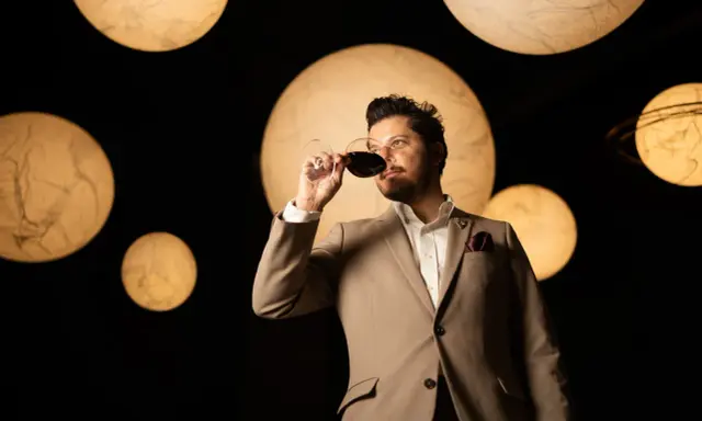 Un homme en costume déguste un verre de vin rouge, entouré de lumières rondes évoquant des planètes. Une dégustation qui rappelle la philosophie du vin biodynamique.