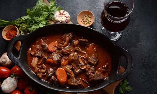 Un plat de vin avec bœuf bourguignon mijoté, garni de carottes et champignons, accompagné d'un verre de vin rouge.