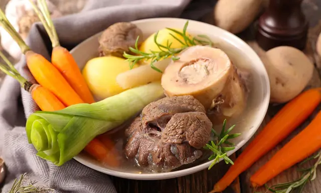 Un plat réconfortant de pot au feu, avec du bœuf, des carottes, des pommes de terre et des poireaux, garni de romarin.