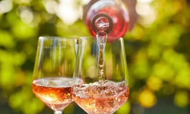Le danger du vin rosé : une bouteille verse son contenu dans deux verres, créant une cascade pétillante sous un soleil radieux.