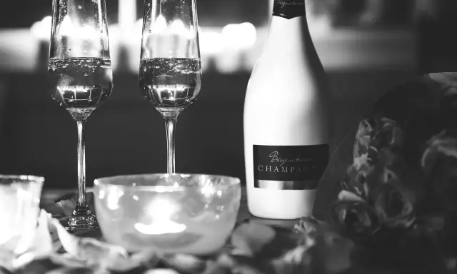 Deux flûtes de champagne pétillant, une bouteille de "Besgane bianc CHAMPAGNE" et des roses, ambiance romantique.