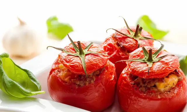 Trois tomates farcies au four, garnies d'une farce savoureuse, servies avec des feuilles de basilic frais.