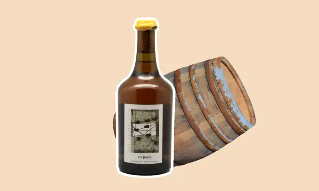 Bouteille de vin jaune à côté d'un vieux fût de chêne. Le vin jaune, une spécialité du Jura, est un vin oxydatif unique.