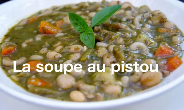 Un bol de soupe au pistou, garni de basilic frais, avec des haricots blancs, des pâtes et des carottes.