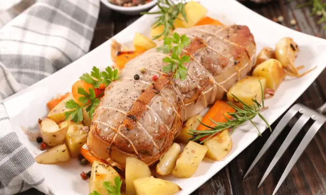 Rôti de veau savoureux, entouré de pommes de terre rôties, carottes et herbes aromatiques, prêt à être dégusté.
