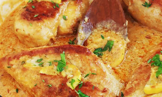 Un délicieux poulet à la crème, garni de persil frais et de rondelles de citron, mijote dans une sauce onctueuse.