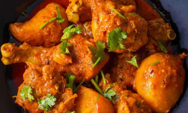 Un plat appétissant de poulet au curry, avec des morceaux de poulet tendres et des pommes de terre dans une sauce épicée, garni de coriandre fraîche.