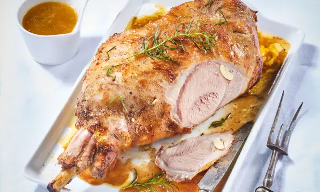 Un gigot d'agneau rôti, doré et juteux, garni de romarin et d'ail, servi avec sa sauce. Un délice à partager.