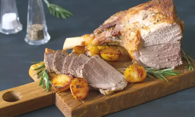 Un gigot de 7 heures, tendre et savoureux, servi avec des pommes de terre rôties et du romarin sur une planche en bois.
