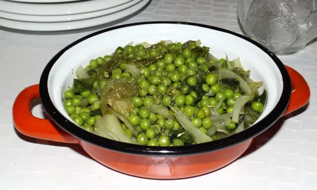 Un plat de petits pois et légumes verts, assaisonnés d'herbes, dans une cocotte orange. Une recette simple et savoureuse.