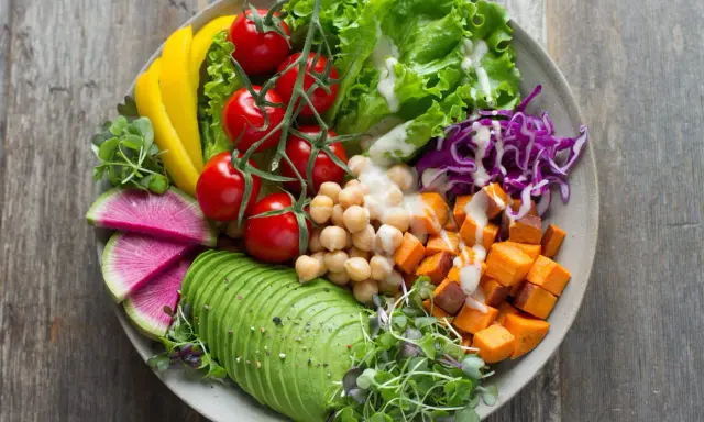 Une assiette colorée avec avocat, tomates, pois chiches, patates douces, chou rouge, radis et poivron jaune. Une belle idée de salade composée.