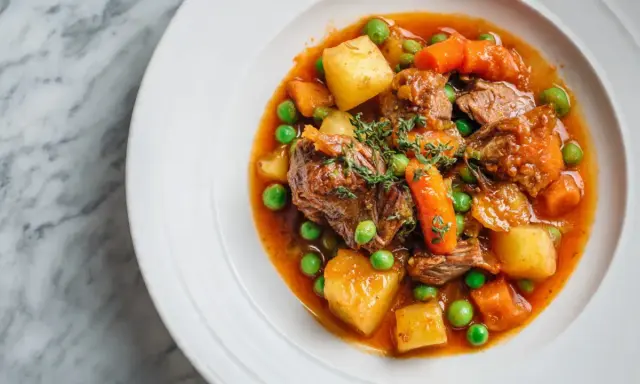 Un savoureux navarin d'agneau recette, garni de pois, carottes et pommes de terre, dans une assiette blanche sur fond marbre.