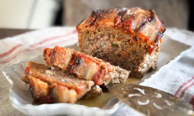 Un délicieux pain de viande, garni de tomates et de lardons, est servi sur une assiette blanche.