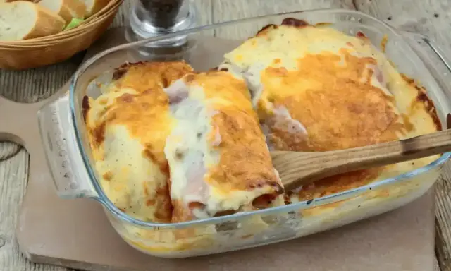 Un plat gratiné de roulés d'endives au jambon, nappés d'une sauce crémeuse et dorée, prêt à être dégusté.