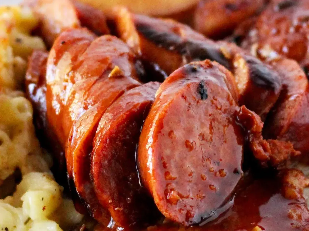 Rougail saucisse, un plat réunionnais savoureux avec des saucisses coupées en rondelles, nappées d'une sauce brune et accompagnées de pâtes.