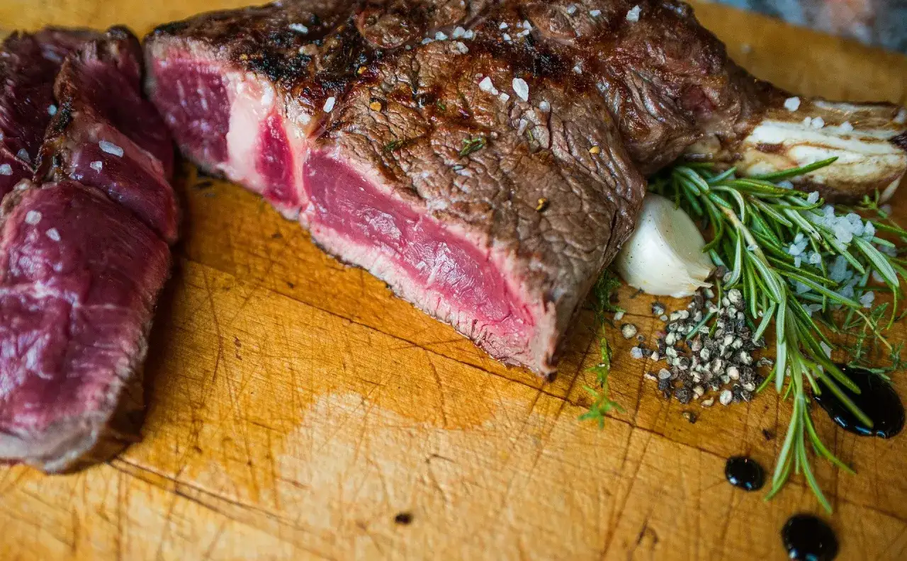 Une c&ocirc;te de b&oelig;uf juteuse, tranch&eacute;e et assaisonn&eacute;e de gros sel, avec du romarin, de l'ail et du poivre sur une planche en bois.