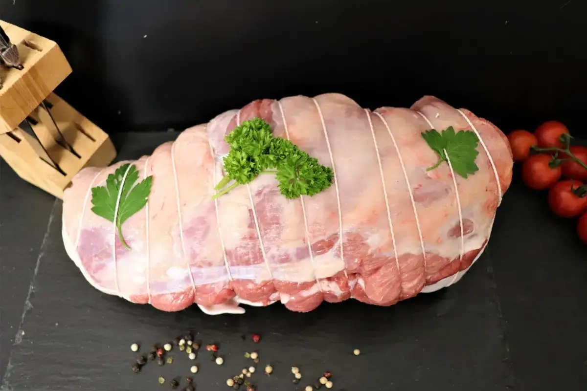 Gigot d'agneau cru, ficel&eacute; et garni de persil, pr&ecirc;t &agrave; &ecirc;tre r&ocirc;ti. Des tomates cerises et des grains de poivre compl&egrave;tent la sc&egrave;ne.