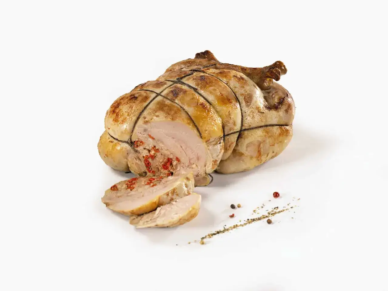 Une pintade au four, dorée et savoureuse, est tranchée, révélant une farce rouge. Des grains de poivre parsèment la présentation.