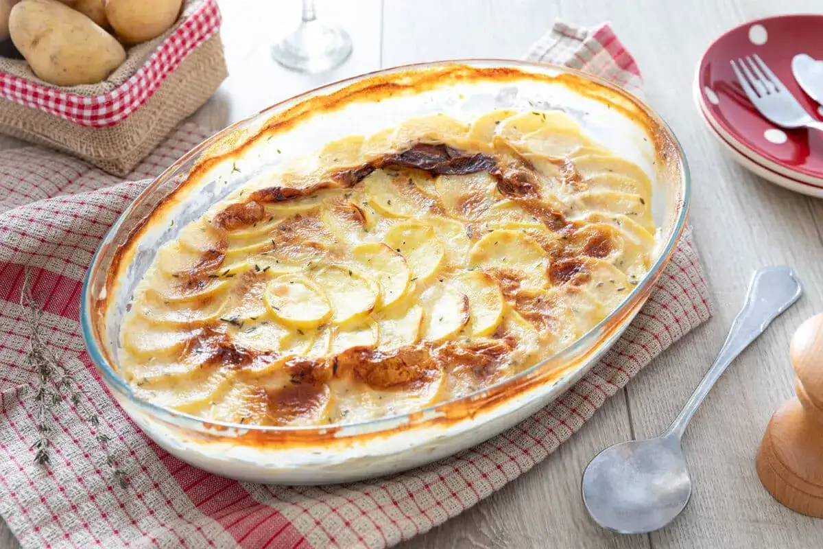 Gratin de pommes de terre crémeux, une recette réconfortante. Des fines tranches de pomme de terre dorées au four, parsemées d'herbes.