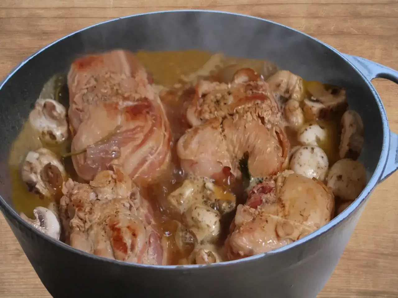 Paupiettes de porc mijotant dans un bouillon savoureux avec des champignons dans une cocotte bleue.
