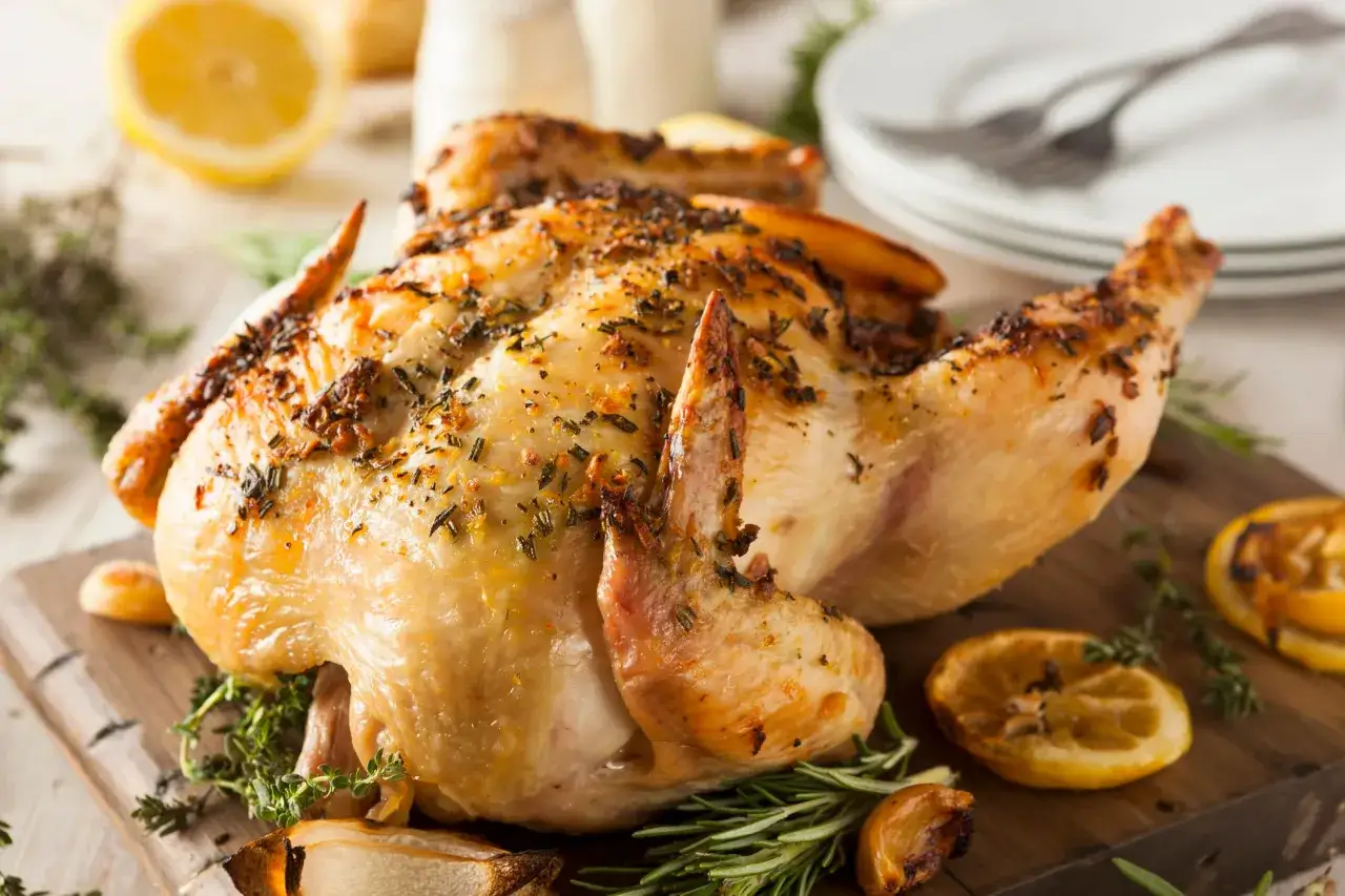 Un délicieux poulet rôti, doré et parfumé aux herbes, est servi sur une planche en bois avec des quartiers de citron et de l'ail rôti.
