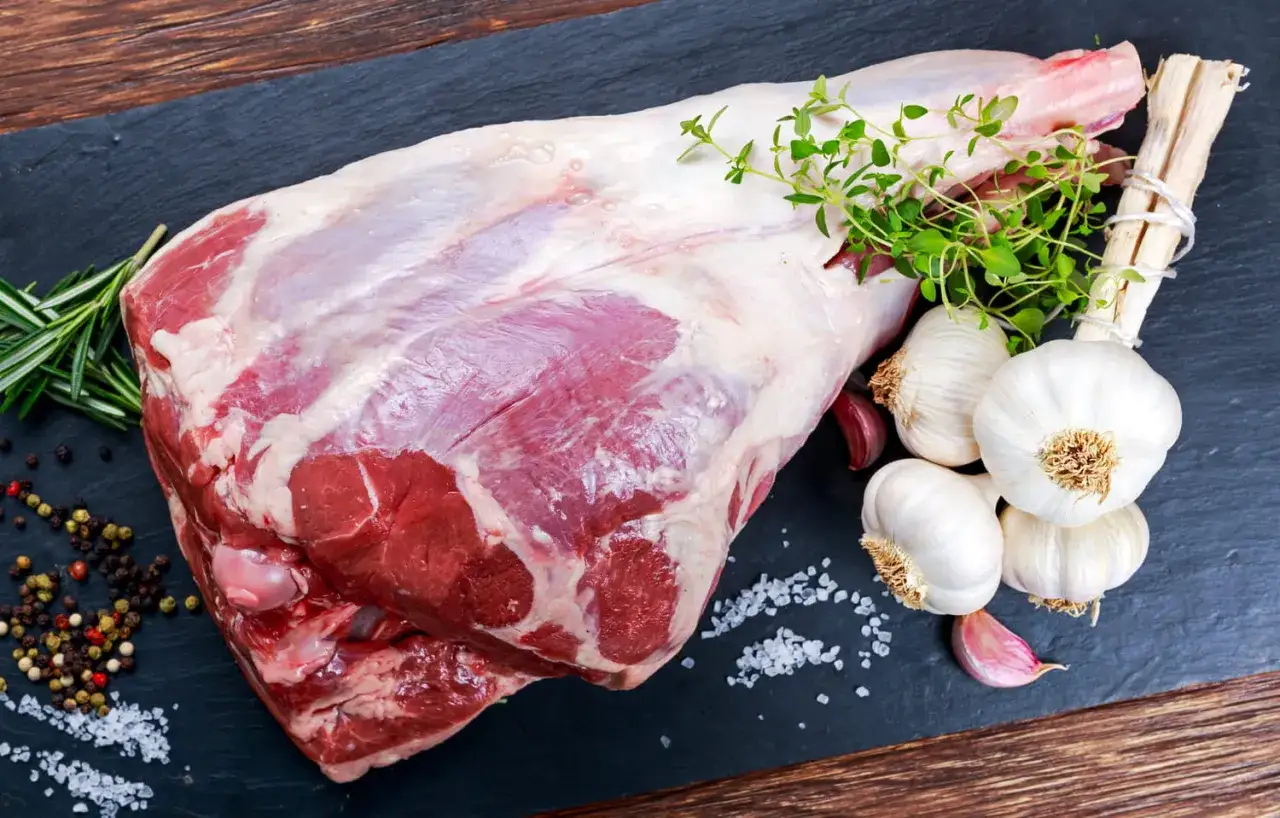 Un gigot de 7 heures cru, pr&ecirc;t &agrave; &ecirc;tre cuisin&eacute;, avec ail, thym et romarin sur une planche d'ardoise.