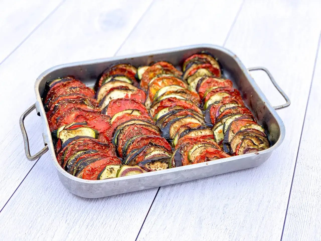 Un plat de tian de courgettes, tomates et aubergines, joliment disposé en éventail dans un plat rectangulaire, prêt à être dégusté.
