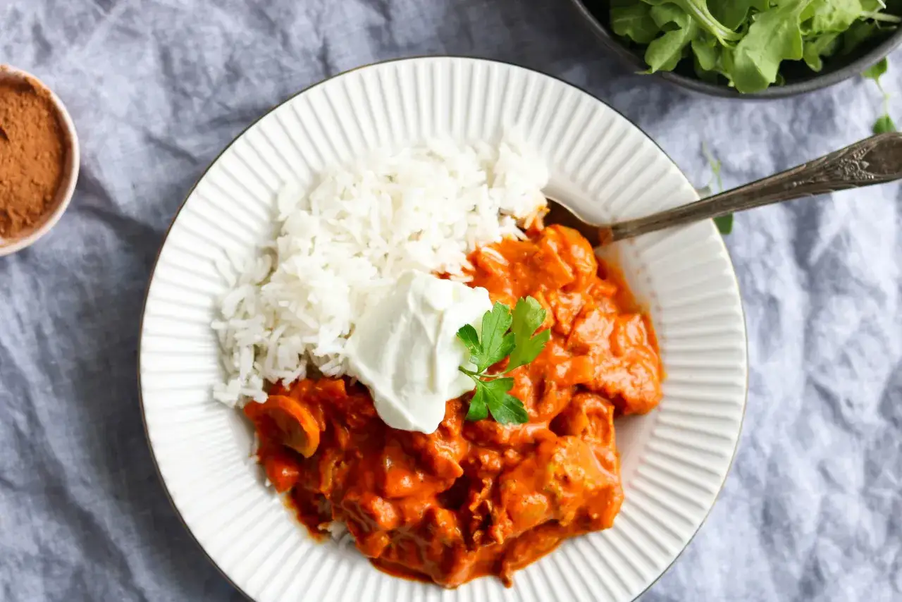 Une assiette de riz blanc avec un poulet au curry crémeux et une touche de persil. Une cuillère est posée sur le plat.