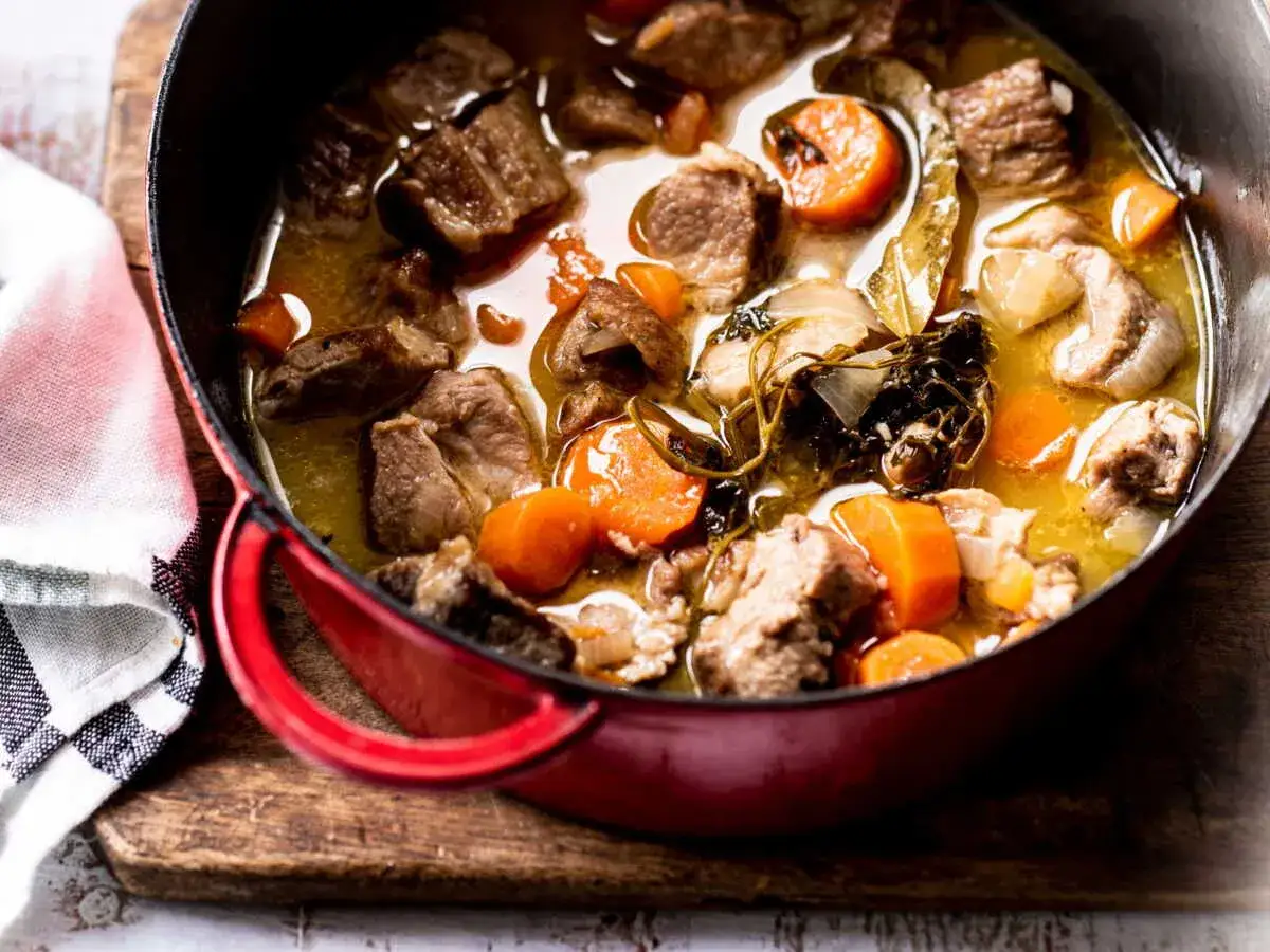 Un savoureux saut&eacute; de porc mijote dans une cocotte rouge, avec des carottes et des herbes aromatiques.