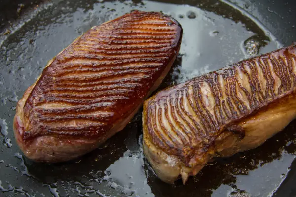 Deux magrets de canard au four, la peau grillée et dorée, baignant dans leur jus de cuisson sur une poêle.