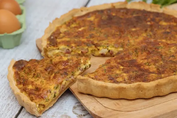 Une part de quiche lorraine dorée, avec sa garniture aux lardons et herbes, prête à être dégustée. La vraie recette quiche lorraine.