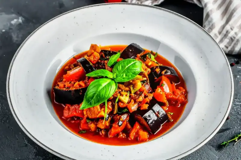 Un plat de ratatouille recette coloré et appétissant, garni de basilic frais, dans une assiette blanche.